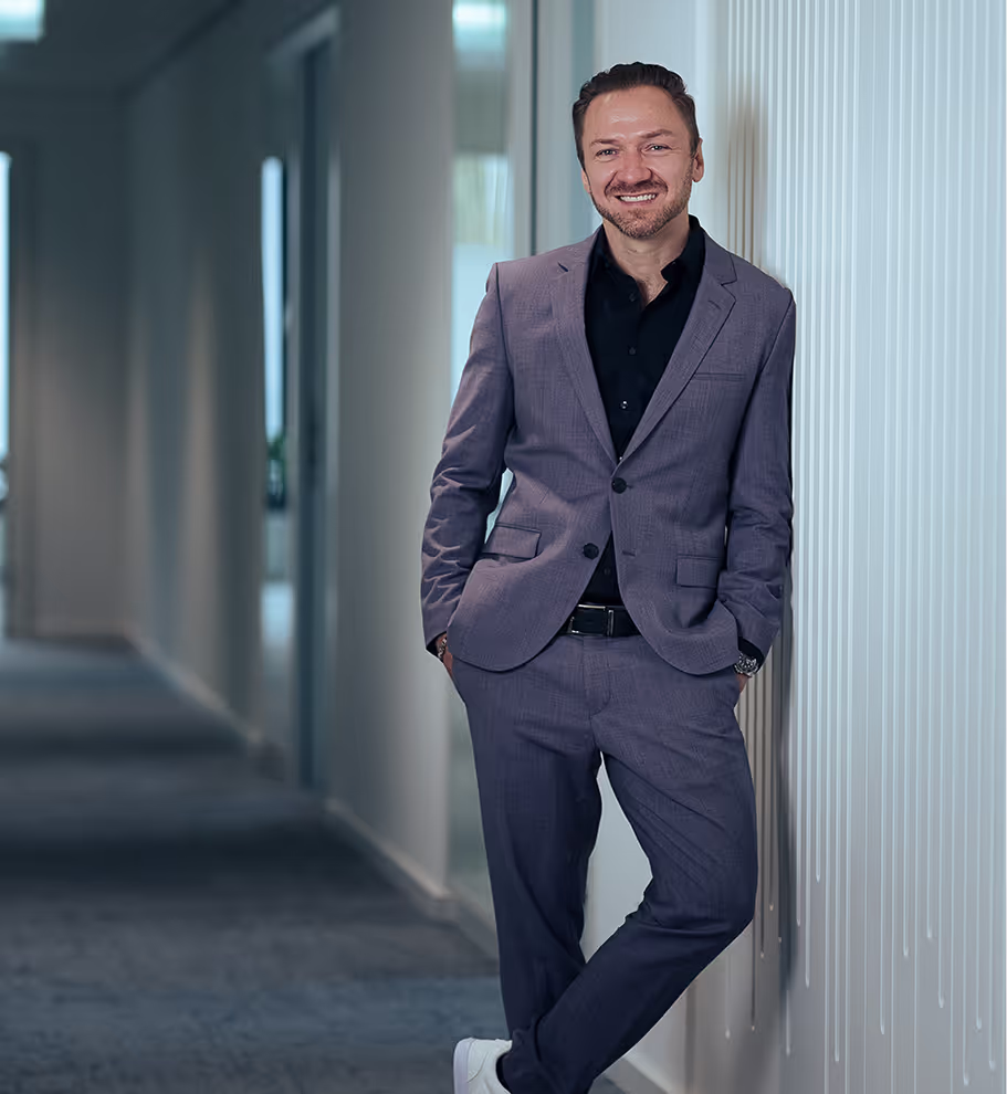 Business & Life Coach Gregor Wojtowicz aus Köln in dunkelblauem Anzug lehnt an einer Wand in einem modernen Büroflur