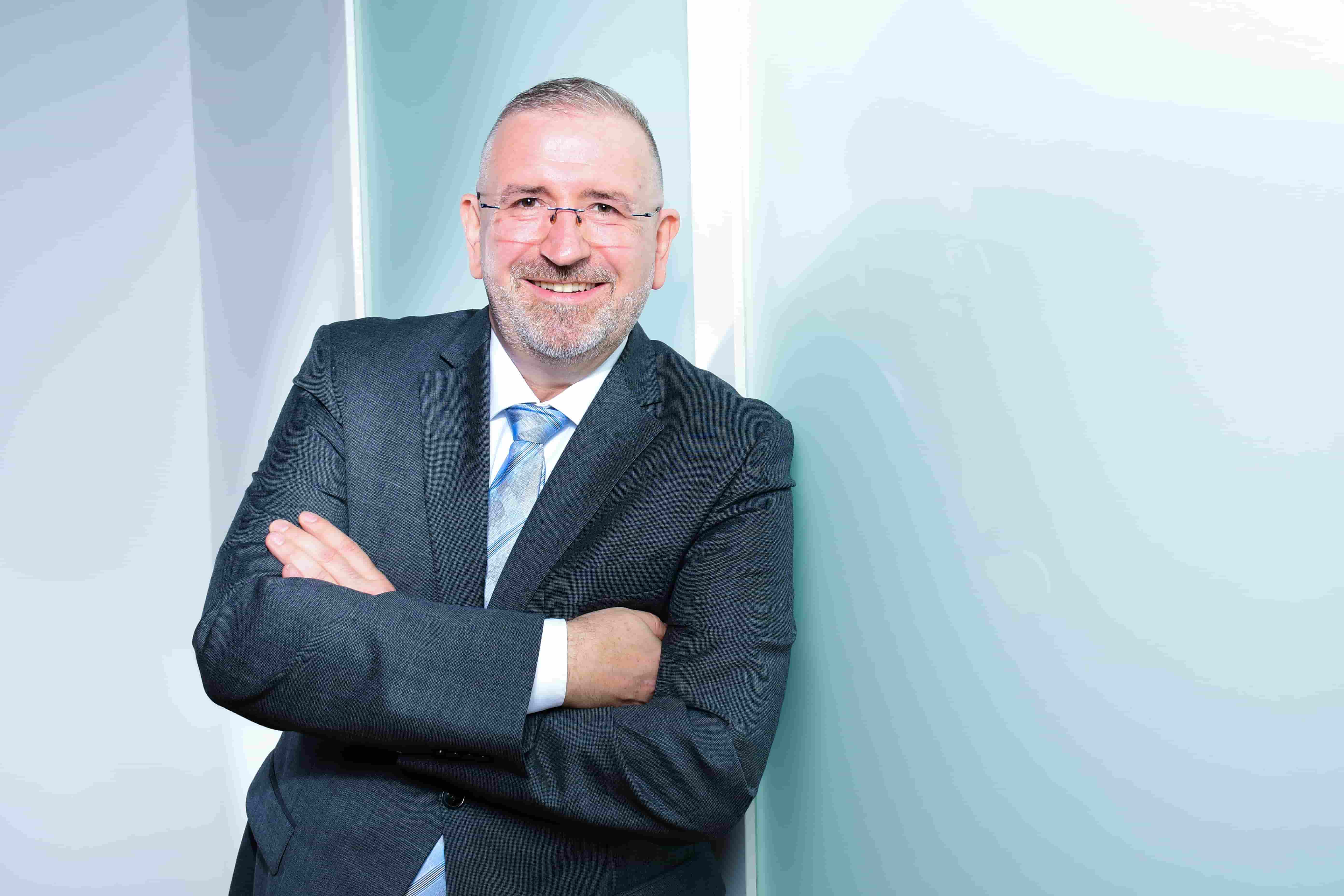 Coaching Klient im dunklen Anzug mit verschränkten Armen vor hellem Hintergrund